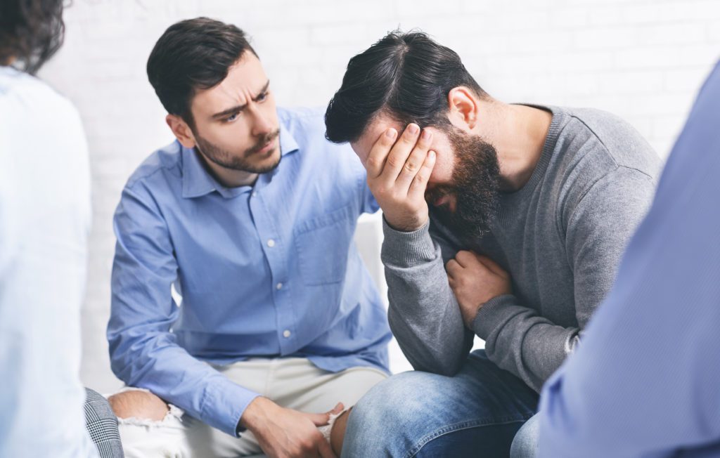 Group members comforting crying addicted man at rehab session